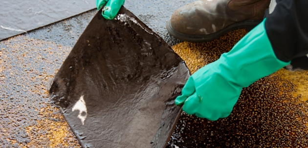 Person holding used oil absorbent mat during spill cleanup